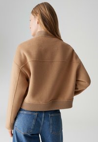 Maglione marrone corto realizzato in tessuto morbido e strutturato con colletto e orlo a coste. Abbinato a jeans blu a vita alta con tasche posteriori.