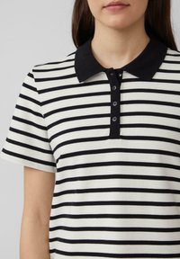 Gestreepte polo shirt met zwart-witte horizontale strepen, een zwarte kraag en zes zwarte knopen bij de hals, gemaakt van een zachte stof.