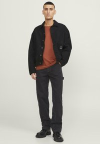 Zwarte denimjas over een roestkleurig T-shirt, gecombineerd met donkere jeans en zwarte laarzen. Eenvoudig ontwerp, effen kleuren, gestructureerde stof.