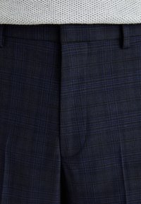 Pantalone u mornarsko plavom karo uzorku imaju teksturiranu tkaninu s suptilnim šarama. Pojas je ravna s remenom.