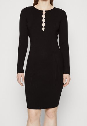 Robe noire en maille côtelée à manches longues avec un col rond et quatre découpes circulaires argentées au centre devant.