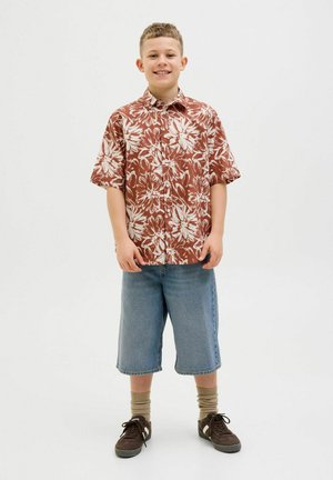 Kurzärmliges, braunes Blumenhemd mit weißen Mustern, kombiniert mit hellblauen Denim-Shorts. Getragen mit braunen Sneakers und beigen Socken.