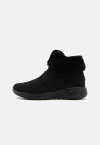 Schwarze Ankle Boots mit Wildleder-Oberfläche, ausgestattet mit einem weichen schwarzen Kunstpelz-Bündchen, runder Zehenpartie und einer Gummisohle mit strukturiertem Grip.