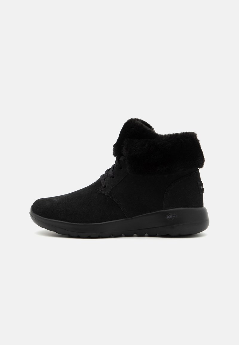 Schwarze Ankle Boots mit Wildleder-Oberfläche, ausgestattet mit einem weichen schwarzen Kunstpelz-Bündchen, runder Zehenpartie und einer Gummisohle mit strukturiertem Grip.