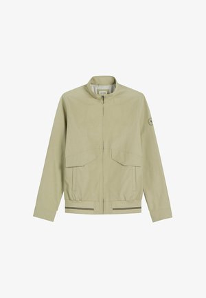 Beżowa kurtka na suwak z dwoma przednimi kieszeniami z klapami, elastycznym paskiem w talii z czarnymi paskami oraz małym okrągłym logo na lewej rękawie.