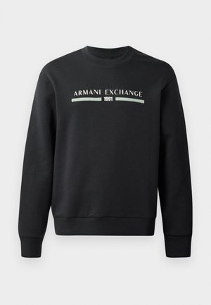 Sweat-shirt noir en tissu doux. Possède un col rond et des manches longues. L'avant affiche "ARMANI EXCHANGE" et "1991" dans des couleurs contrastantes.