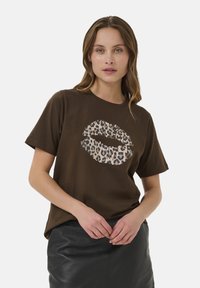 Hnědé bavlněné tričko s potiskem rtěnky s leopardím vzorem na přední straně. Krátké rukávy, volný střih a měkká textura.