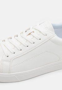 Zapatilla blanca de cuero con textura suave, con cordones planos blancos, suturas sutiles y una suela de goma de perfil bajo.