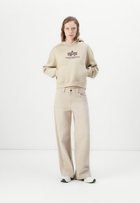 Felpa beige con cappuccio e logo abbinata a pantaloni beige a gamba larga, completata da scarpe sportive bianche e verdi. Tessuto dal tocco morbido.