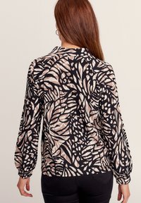 Langärmlige Bluse aus strukturiertem Stoff mit einem schwarzen und beigen Blumenmuster. Rundhalsausschnitt, Ballonärmel und lockere Passform.