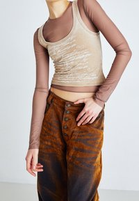 Beige linne med tryckt text, lager-på-lager över en brun långärmad skjorta. Bruna kordfloretbyxor med knappstängning framtill och ett subtilt mönster.