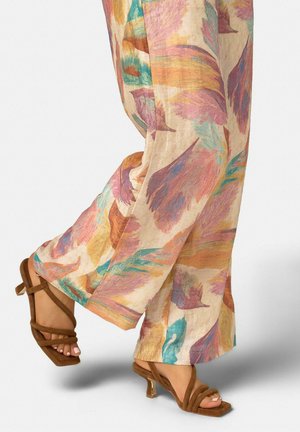 Pantalon à jambes larges avec motifs de plumes colorées en rose, orange, bleu et vert, porté avec des sandales à talons brunes à brides.