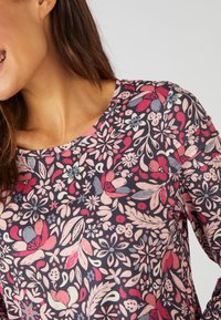 Maglietta a maniche lunghe su sfondo scuro con un motivo floreale colorato che presenta fiori e foglie rossi, rosa, blu e verdi. Collo rotondo.