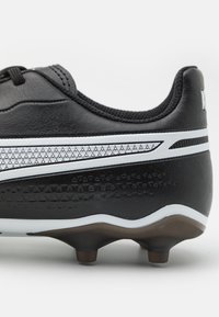 Scarpa da calcio nera con una parte superiore testurizzata, accenti bianchi e suola in gomma stampata. Presenta un motivo triangolare sollevato lungo il lato.