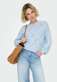 Pull bleu clair en maille avec des découpes en forme de losange, manches longues et encolure arrondie. Assorti à un jean délavé clair et un sac en cuir marron clair.