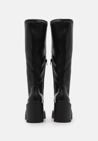 Czarne skórzane kozaki za kolano o gładkiej fakturze, z bocznymi zamkami błyskawicznymi i masywną podeszwą. Posiadają wzmocnione szwy i minimalistyczne akcenty.