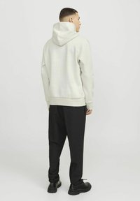 Light gray hooded sweatshirt with a relaxed fit, ribbed cuffs, and waistband. Black tapered pants and black shoes complete the outfit.
