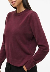 Burgundowa sweter o miękkiej fakturze z okrągłym dekoltem i długimi rękawami, charakteryzujący się skróconym fasonem w talii oraz prążkowanymi mankietami.