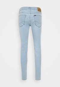 Světle modré skinny džíny s hladkou denimovou texturou, obsahující koženou nášivku na zadním pase a dvě zadní kapsy.