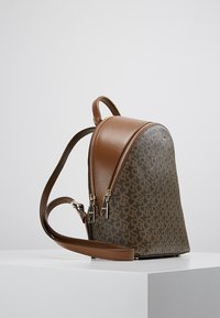 Textured brown leather backpack with a geometric pattern, featuring double zippers, a rounded top, and a single adjustable shoulder strap.