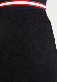 Svart spetskjol med blommönster, bärs tillsammans med en marinblå topp med vita och röda horisontella ränder vid midjan.