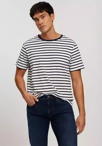 Pasiasta koszulka w białym i granatowym kolorze, z okrągłym dekoltem, krótkimi rękawami i luźnym krojem, połączona z ciemnoniebieskimi dżinsami.