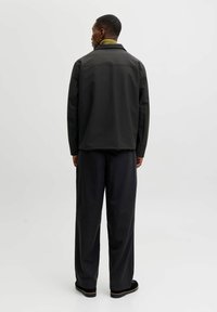 Čierna bunda so štruktúrovaným dizajnom a golierom, skombinovaná s širokými čiernymi nohavicami. Obsahuje zelený rebrovaný golier a textúrovanú látku.