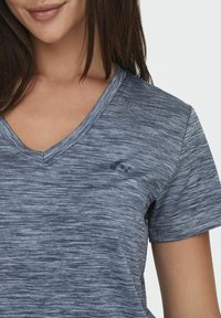 T-shirt z dekoltem w serek w heatherowym ciemnoniebieskim kolorze; krótki rękaw; posiada mały nadruk logo po lewej stronie klatki piersiowej.