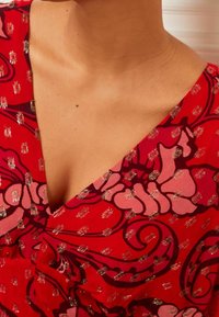 Robes florales rouges avec un décolleté en V profond, des manches courtes et des accents métalliques. Le tissu a une texture lisse avec des motifs élaborés.