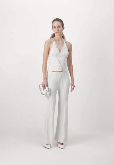 Haut halter en tricot côtelé blanc avec des détails en dentelle, associé à un pantalon évasé. Accessoirisé avec un sac blanc à anse en chaîne.