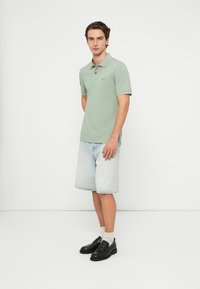 Jasnozielona koszulka polo z krótkim rękawem, zestawiona z jasnoniebieskimi szortami z denimu. Noszona z czarnymi mokasynami i kremowymi skarpetkami.