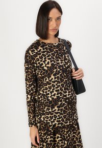 Langermet topp med leopardmønster i brunt og svart, med rund hals og løs passform, sammen med en liten svart håndveske.
