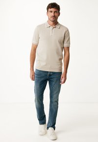 Beige polo triko s krátkým rukávem a bílým lemováním, doplněné modrými džíny a bílými teniskami. Pohodlný střih a jednotná textura.