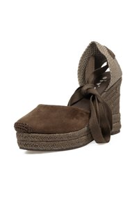 Zapato de tacón cuña de ante marrón con suela de yute trenzado estilo espadrille, que presenta una correa de tobillo entrecruzada y un diseño de punta redonda.
