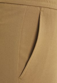 Tessuto marrone con una texture liscia presenta una tasca laterale. Il design include cuciture ordinate e una leggera lucentezza.