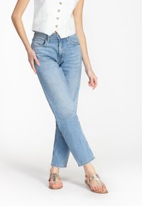 Jeans in denim azzurro chiaro con taglio dritto, dotati di tasche anteriori e chiusura con zip. Indossati con sandali metallici con cinturini.