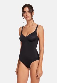 Svart bodysuit med justerbara remmar, formar kopp och en figurnära design. Slät textur med låg rygg och benöppningar.