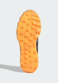 Sole sportovní obuvi s texturovaným oranžovým gumovým povrchem a hlubokými vzory, navržený pro trakci a odolnost.