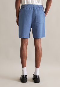 Blauwe, getextureerde shorts met een elastische tailleband en een achterzak. Draagt zich met zwarte schoenen en witte sokken. Eenvoudig ontwerp, tot de knieën.