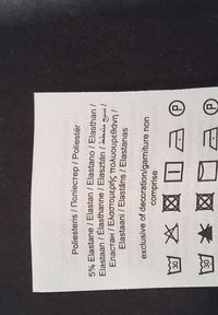 Tygetikett som visar innehållet 95% polyester, 5% elastan på flera språk, tillsammans med tvätt- och skötselsymboler.
