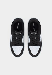 Ζευγάρι μαύρα και άσπρα αθλητικά παπούτσια Champion με κορδόνια, αποτυπωμένα από ψηλά σε απλό φωτεινό φόντο.