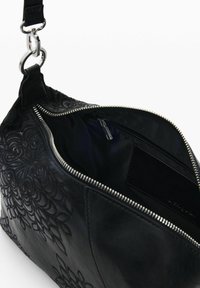 Mustast nahast käekott reljeefse lillemustriga, osaliselt avatud hõbedane tõmblukk, mis paljastab musta kangast voodri ja sees väikese tõmblukuga tasku.