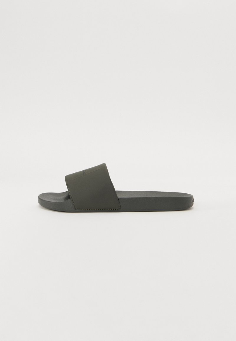 Temno siva drsna sandal s eno široko naramnico in ravnim podplatom. Narejena iz gumijastega materiala, s gladko teksturo in minimalnim dizajnom.