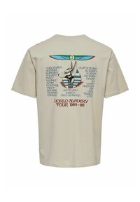 Camiseta de algodón beige con un diseño gráfico que presenta un ankh y un texto que enumera países, "Gira Mundial de Esclavitud 1984-85," en la parte posterior.