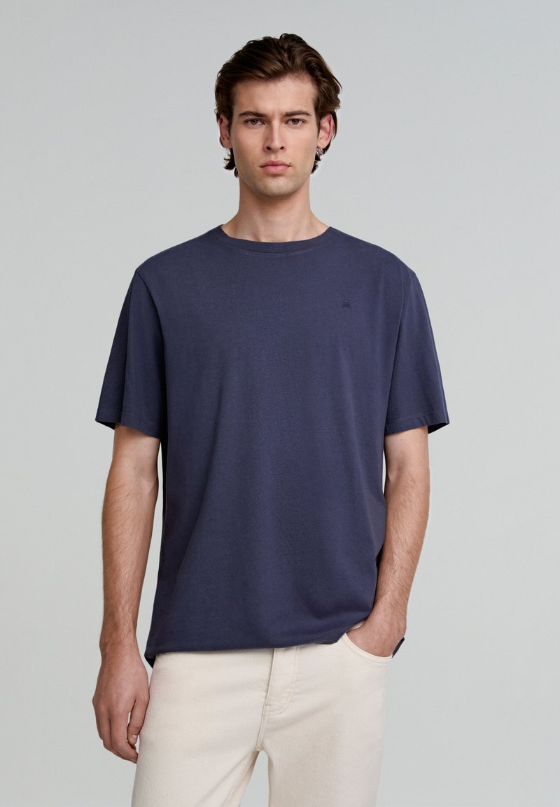 Marineblauwe t-shirt met korte mouwen van zachte stof, met een ronde hals en een subtiele logo op de linkerborst, gecombineerd met lichte broek.