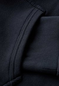 Donkerblauwe sweatshirtstof met ribbelmanchetten. Close-up weergave die de gladde textuur en nette stiksels laat zien. Zacht, elastisch materiaal.