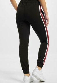 Svart joggebukser med elastisk midje, med sidestreker i hvitt og burgunder. Avsluttet med ribbede mansjetter og brukt med hvite sneakers.