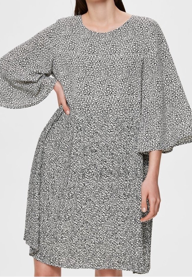 Robe à motifs floraux en noir et blanc avec un col rond, des manches évasées fluides et une taille froncée. Texture du tissu douce.