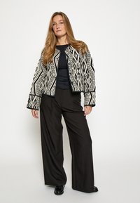 Teksturowana kurtka w czarno-białe wzory z geometrycznymi motywami, w połączeniu z luźnymi czarnymi spodniami i dopasowaną bluzką.