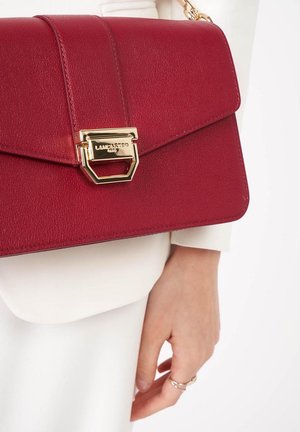 Borsa a mano in pelle rossa con un design strutturato, hardware dorato e chiusura a patta con dettaglio a chiusura geometrica.